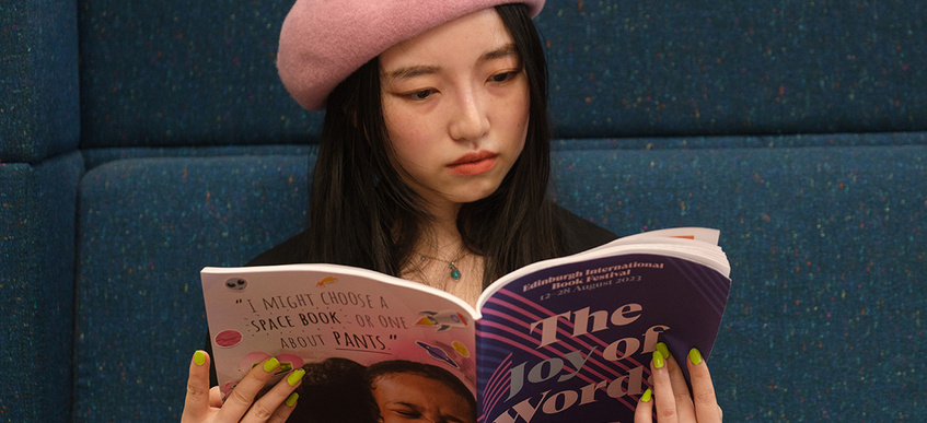 Young woman in colourful hat reading Book Festival brochure